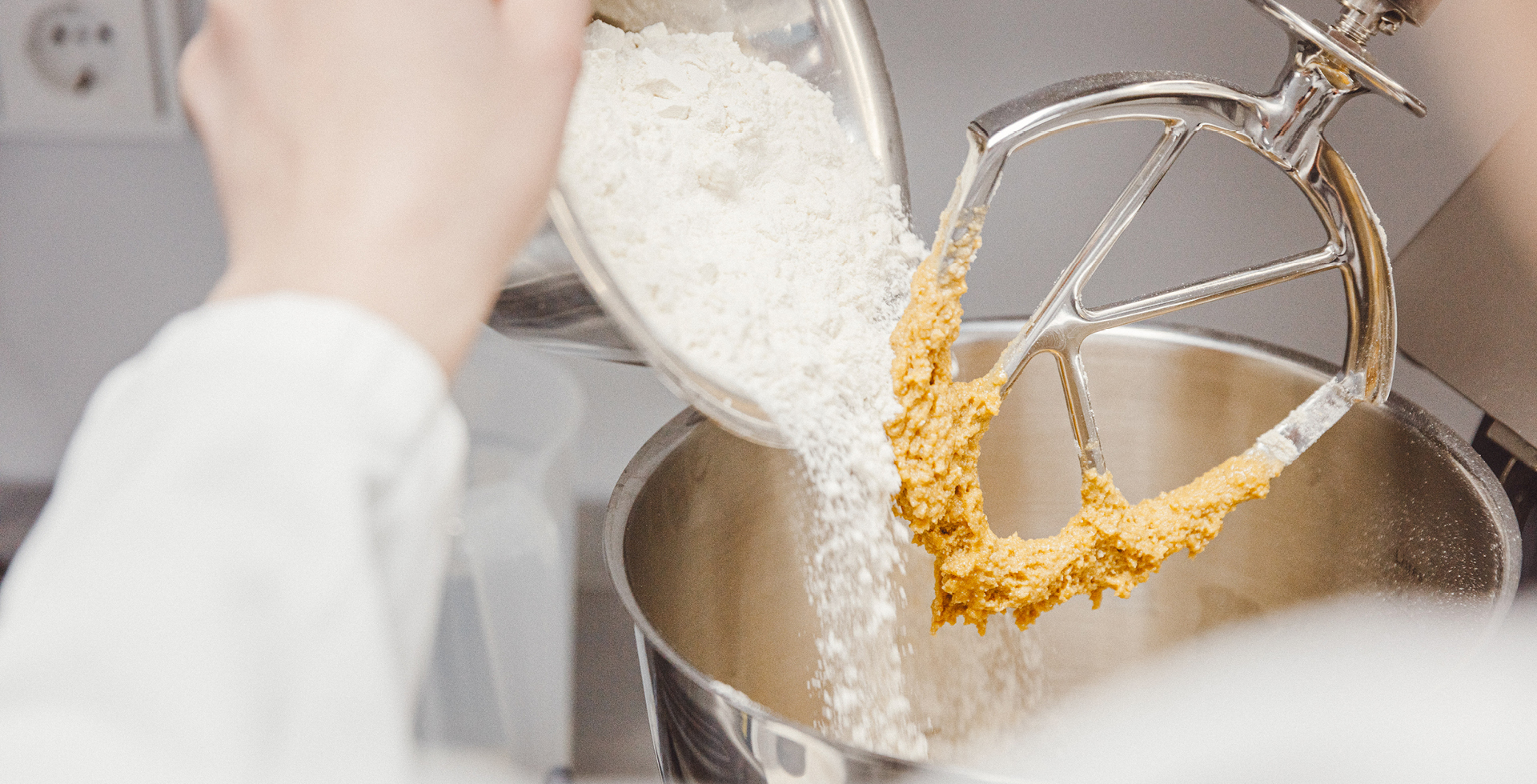 Mehl wird in eine Küchenmaschine mit Rührwerk gegeben, in der bereits ein gelblicher Teig angerührt wird.