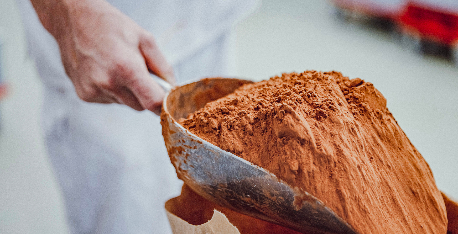 Kakaopulver wird von einer Hand mit einer Schaufel aus einem Papiersack entnommen
