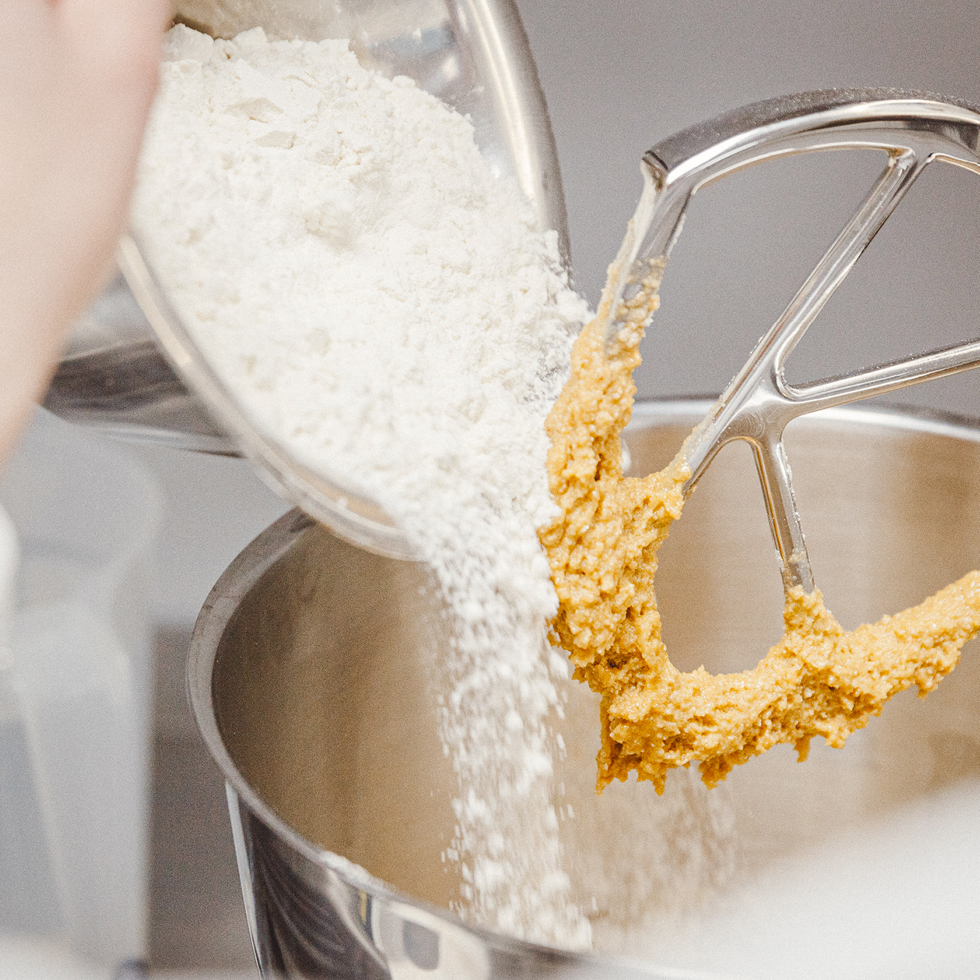 Mehl wird in eine Rührschüssel gegeben. Ein Knethaken mit Teig ist zu sehen.