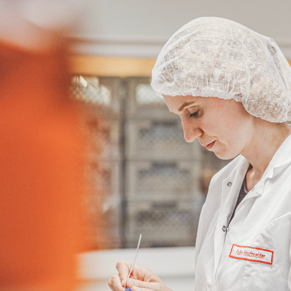 Eine Mitarbeiterin mit Haarnetz und Kittel bekleidet