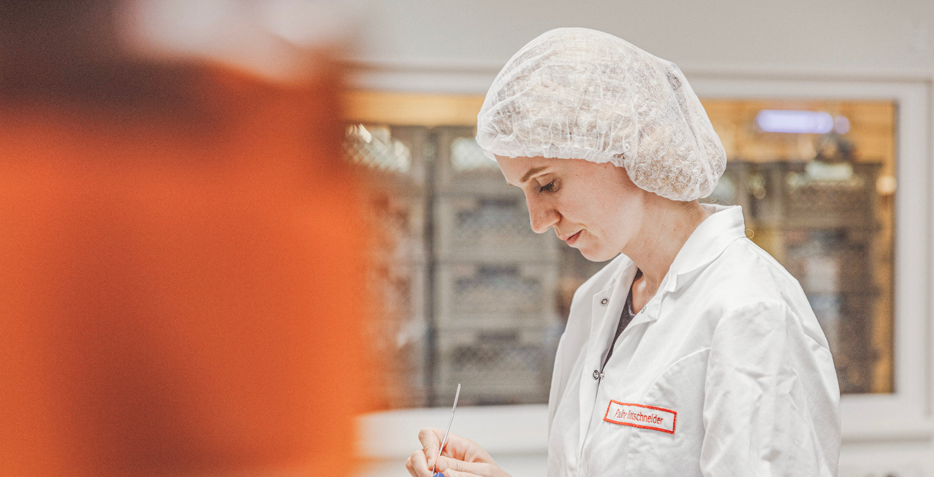 Eine Mitarbeiterin mit Haarnetz und Kittel bekleidet